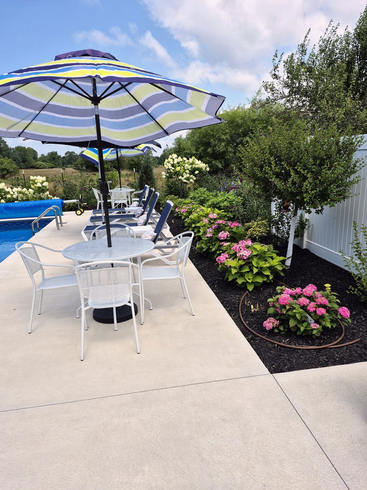 Poolside patio table with umbrella, lounge chairs, and flower borders